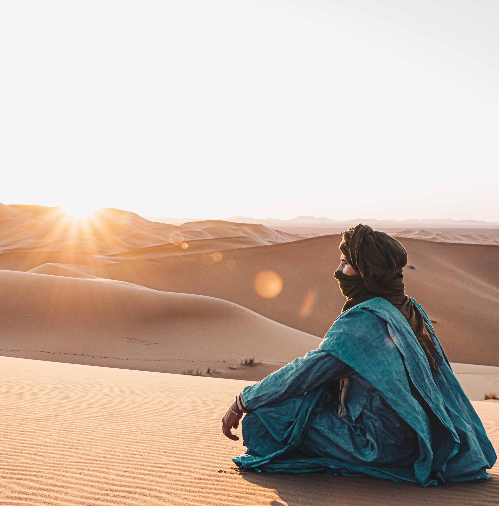 A women sits in the Moroccan desert admiring the setting sun while on tour