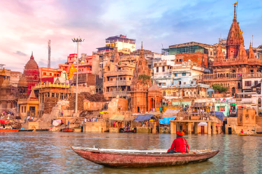 A photo of the Ganges river in India with the village in the back and a person in a boat in the front