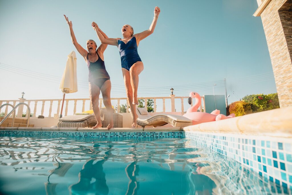 Two women jump into a pool while on vacation with Womens Travel Network