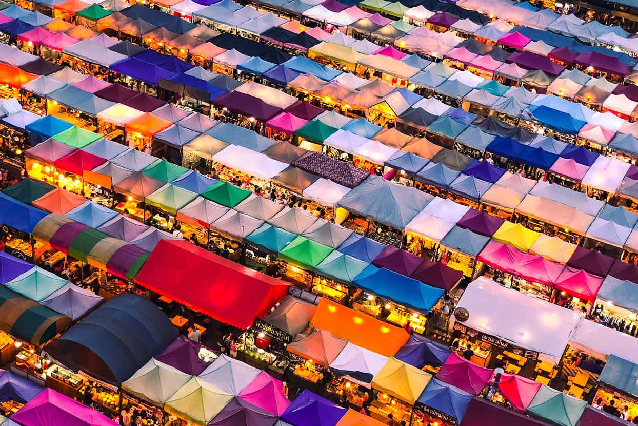An aerial view of a marketplace in Thailand, showing many colours of fabric roofs.