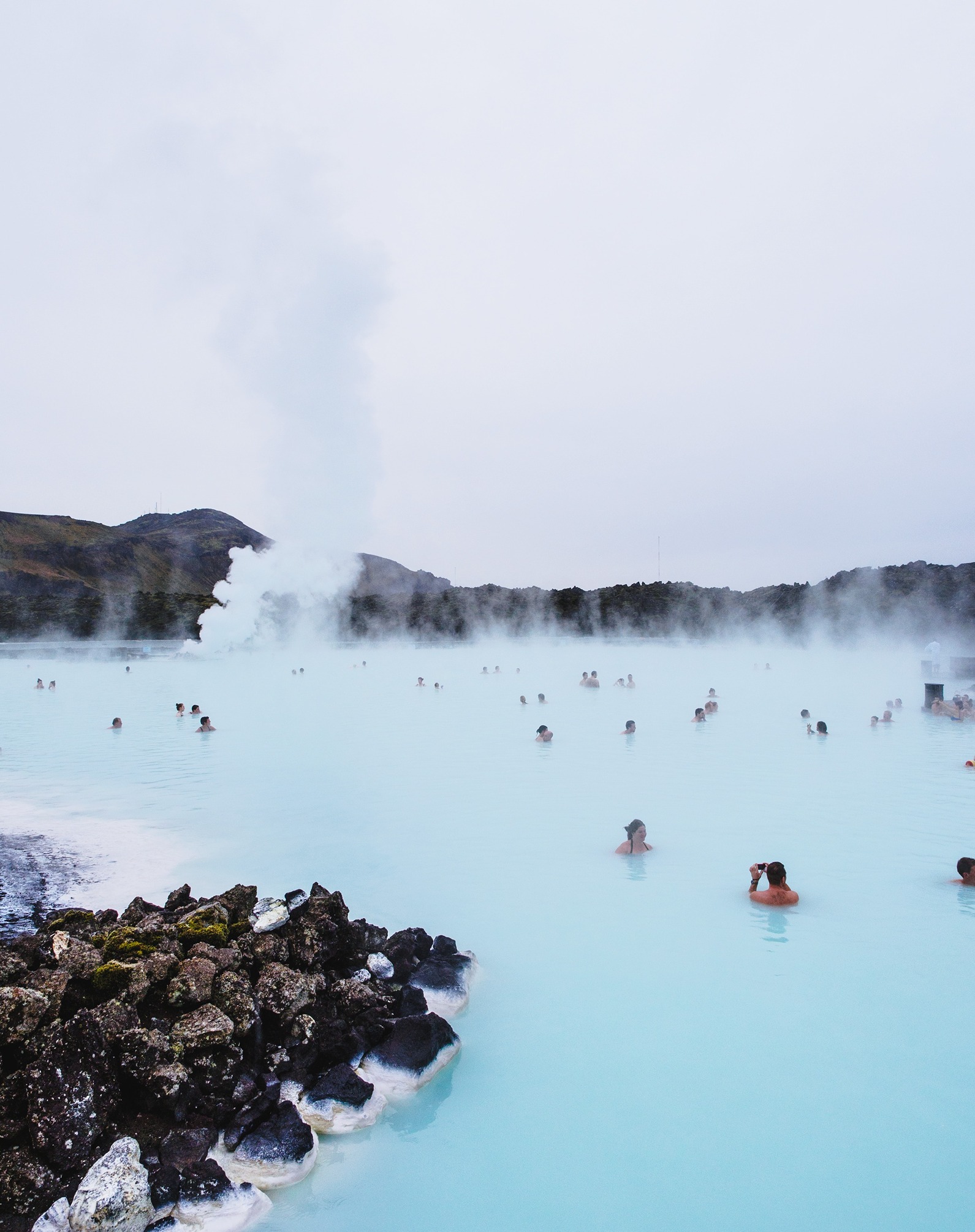 A large light blue coloured thermal bath in Iceland with people bathing and relaxing inside