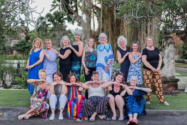 A bunch of happy ladies pose together and smile in front of lush trees and garden during Womens Travel Network's Bali tour for women.